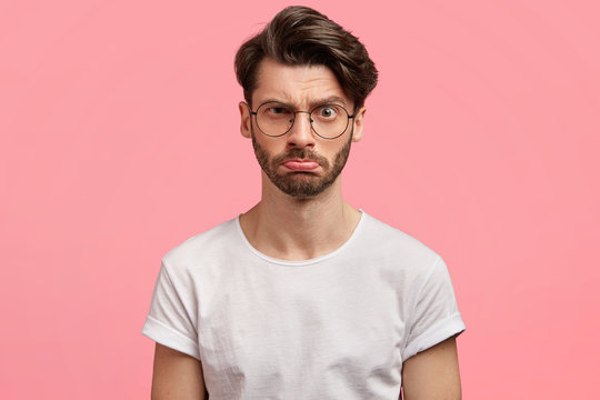 Serious discontent stylish male freelancer with unhappy expression, wears round spectacles, being annoyed with bad internet connection, expresses negative emotions and feelings. Displeasure.