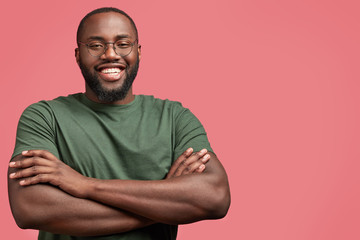 Waist up portrait of handsome young male with satisfied expression, keeps arms folded, has shining...
