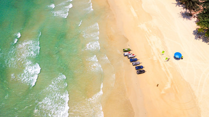 Aerial : Bird eye view of sea waves  against the sand beach coast line and overhead view of a water scooter rental point under blue umbrella