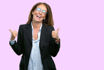 Middle age business woman smiling broadly showing thumbs up gesture to camera, expression of like and approval