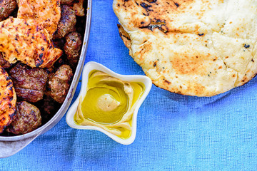 Delicious hummus with fresh olive oil in a white bowl, pita or pitta bread and bbq meat-kebabs and steak. Traditional Middle Eastern cuisine.Delicious Food served on Blue vintage tablecloth background