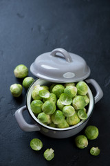 Pot with raw fresh brussels sprouts, high angle view on a black stone background, vertical shot with copyspace
