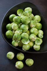 Closeup of fresh uncooked brussels sprouts in a black bowl, selective focus, vertical shot