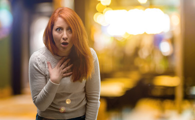 Beautiful young redhead woman happy and surprised cheering expressing wow gesture at night