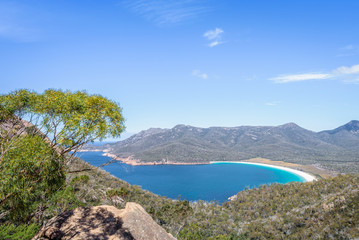 Fototapeta na wymiar Wonderful view to stunning sandy beach blue turqouise water on warm sunny day with blue sky relaxing after hiking on top Mount Amos, Wineglass, Freycinet National Park, Coles Bay, Tasmania, Australia