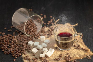 Hot coffee and sugar cube with roasted coffee beans on wood table