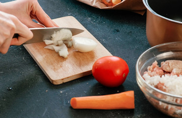 Closeup woman's hands cutting an onion on a wood board.