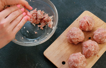 Close-up of a woman's hands making meatballs of minced meat with rice and put it on a wooden board. Top view.