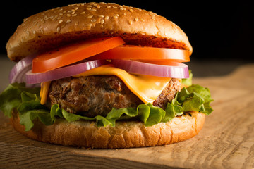 Home made hamburger with beef, onion, tomato, lettuce and cheese. Fresh burger close up on wooden rustic table with potato fries, beer and chips. Cheeseburger.
