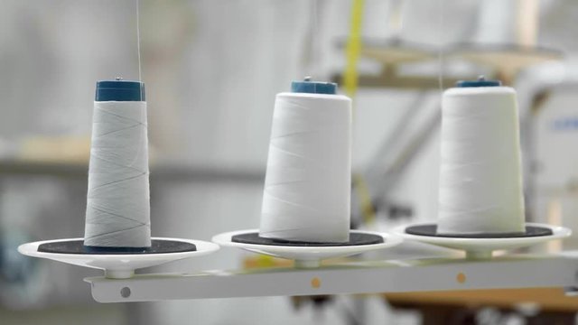 Closeup of three big bobbins with thin white thread on working professional sewing machine. Real time full hd video footage