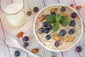 Oatmeal porridge.Breakfast cereals with blueberries and glass of milk on vintage white wooden table.Healthy eating