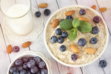 Oatmeal porridge.Breakfast cereals with blueberries and glass of milk on vintage white wooden table.Healthy eating