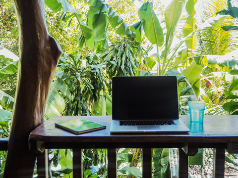 laptop of a digital nomad on a wooden table in nature with a green tropical background