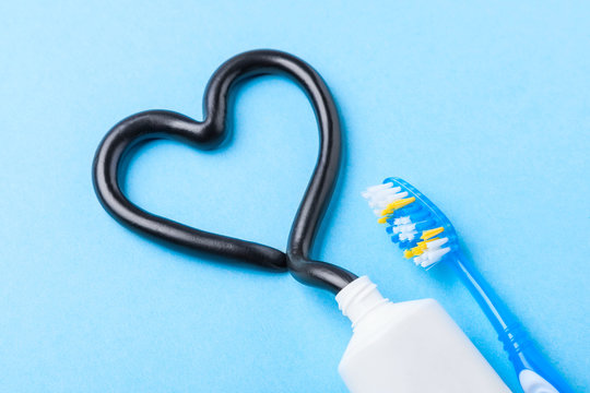 Black toothpaste from charcoal for white teeth. Tooth-paste in the form of heart, tube and toothbrush on blue background.