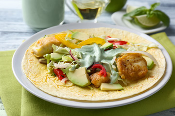 Plate with tasty fish taco and creamy sauce on kitchen table