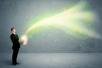 Fototapeta premium Bright yellow, green light beams escaping a cardboard box held by young elegant male business person in stylish suit concept.