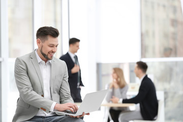 Portrait of handsome young businessman with laptop in office