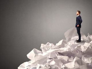 Thoughtful young businessman standing on a pile of crumpled paper with a deep grey background