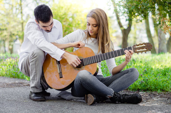 Young Girl Learning Guitar From Male Teacher Outdoors.