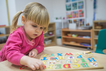 Fototapeta premium Little caucasian girl playing with wooden puzzle and space for text