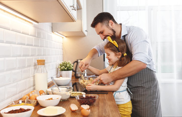 happy family in kitchen. Father and child daughter knead dough and bake biscuits