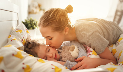 mother wakes her daughter in bed in  morning