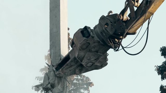 Close-up of demolition machine biting ruins of abandoned building, iron tool