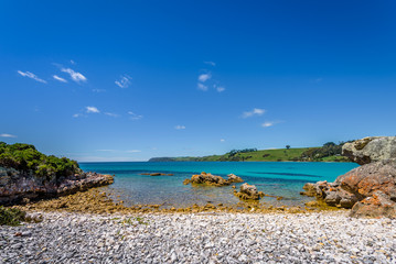 Pretty view to small paradise like town village sandy beach with turquoise blue water and red orange rocks and green shore forest on warm sunny clear sky day, Boat Harbour Beach, Tasmania, Australia