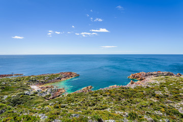 Fototapeta na wymiar Stunning view from bright white light station to deep blue sea ocean bay turquoise water with orange red rocks at shore coast on warm sunny clear sky day, Rocky Cape National Park, Tasmania, Australia