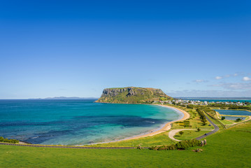 Stunning view point to big old volcanic rock mountain top called The Nut with blue turquoise water beach bay and green grass lands on warm sunny clear sky day, Stanley, North-West, Tasmania, Australia
