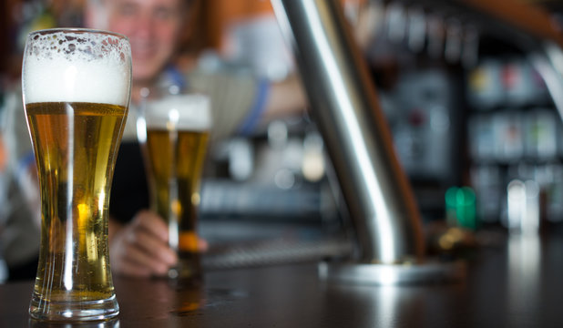 glass of beer on bar counter against background of friendly bartender