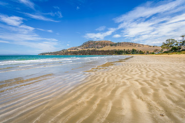 Beautyful view to small paradise like sandy waves beach with turquoise blue water and shore mussels coast stripes mountains on warm sunny clear sky day, Seven Miles Beach, Hobart, Tasmania, Australia
