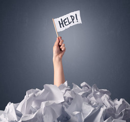 Female hand emerging from crumpled paper pile holding a white flag with help written on it