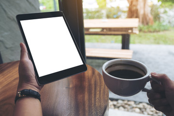 Mock up image of hands holding black tablet pc with white blank screen while drinking coffee in cafe