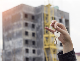 A girl in her hand holds the keys to an apartment on the background of a built house