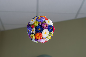 Multicolored artificial flowers collected in a ball weigh on the ceiling.