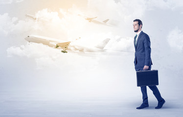 Obraz premium Elegant businessman going somewhere with briefcase and airplane on the background 