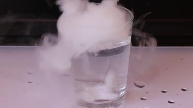 The water in glass and put dry ice inside and engender white smoke on white floor with black background.