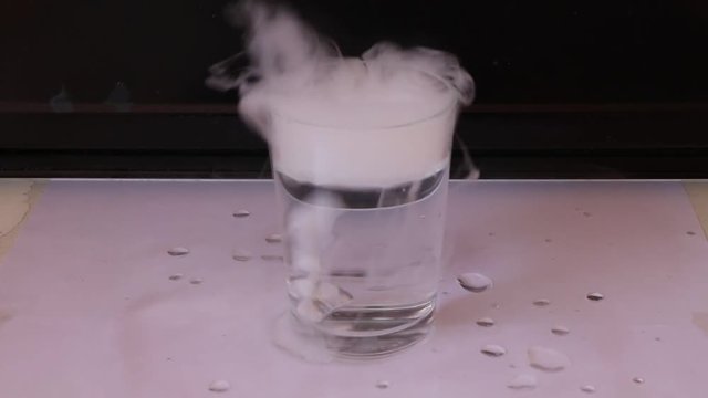 Dry ice in a glass of water and engender white smoke on white floor with black background.