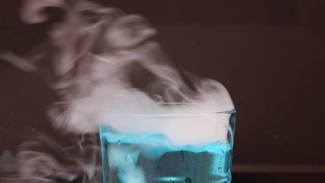 Dry ice in a glass of blue water and engender white smoke on black background.