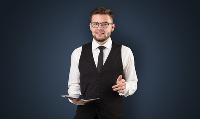Handsome spectacled businessman holding a tablet with dark background
