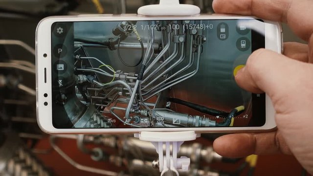 Point of view. A man's hand takes a snapshot of a jet engine using a modern smartphone and a self-device for selfie.