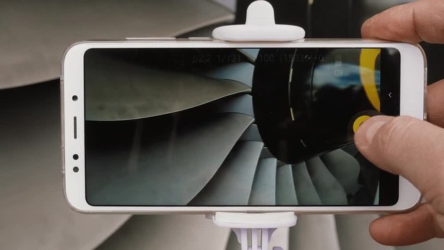 A man engineer photographs a jet engine. The man's hand takes a picture of the engine of the aircraft, using a modern smartphone and a monopod for selfie.