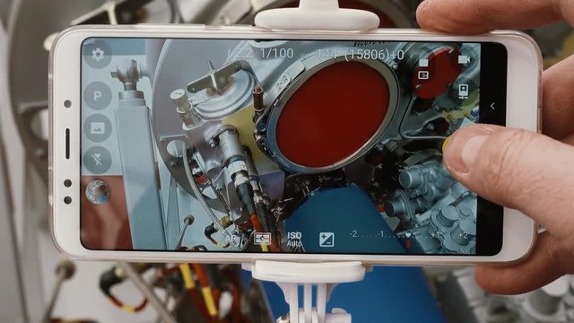 Point of view. A man's hand takes a snapshot of a jet engine using a modern smartphone and a self-device for selfie.