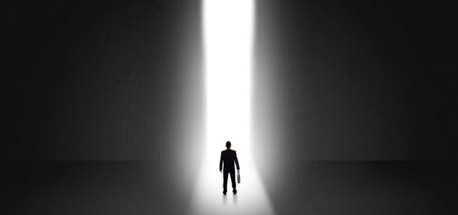 Businessman standing and seeing the light at the end of a big wall
