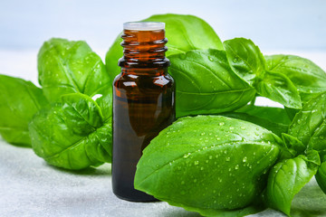 Leaves of basil and a small bottle of oil on a concrete table.