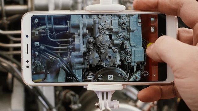 A man engineer photographs a jet engine. The man's hand takes a picture of the engine of the aircraft, using a modern smartphone and a monopod for selfie.