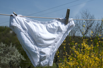 Fototapeta na wymiar Ladies white lace panties hanging to dry closeup on rope in country yard on nature and sky background