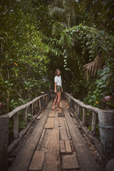Fototapeta na wymiar Traveling girl on the wooden bridge. Pretty young woman in the jungle. Summer lifestyle and adventure photo