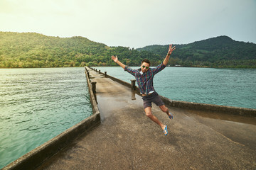 Naklejka premium Traveling boy on the pier. Pretty young man jumping on the bridge. Summer lifestyle and adventure photo